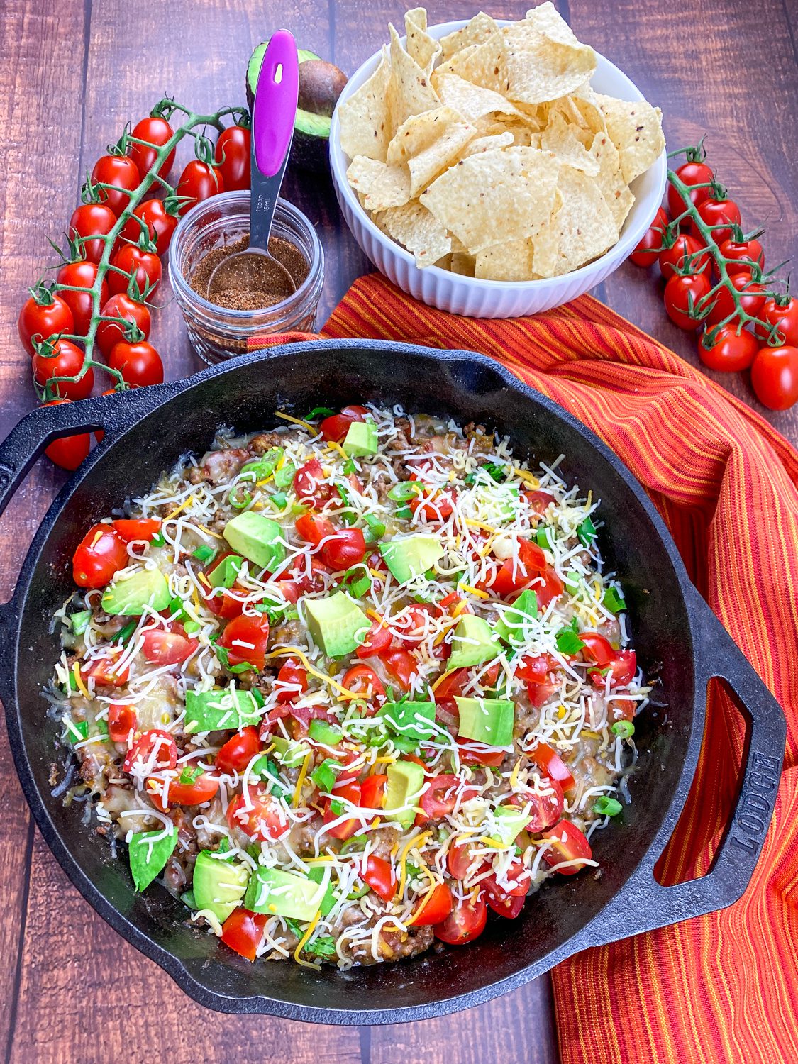 Cheesy beef taco skillet in a cast iron pan with fresh toppings and tortilla chips on the side.