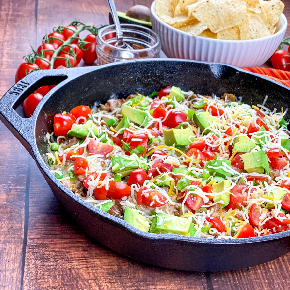 Cheesy beef taco skillet in a cast iron pan with fresh toppings and tortilla chips on the side.