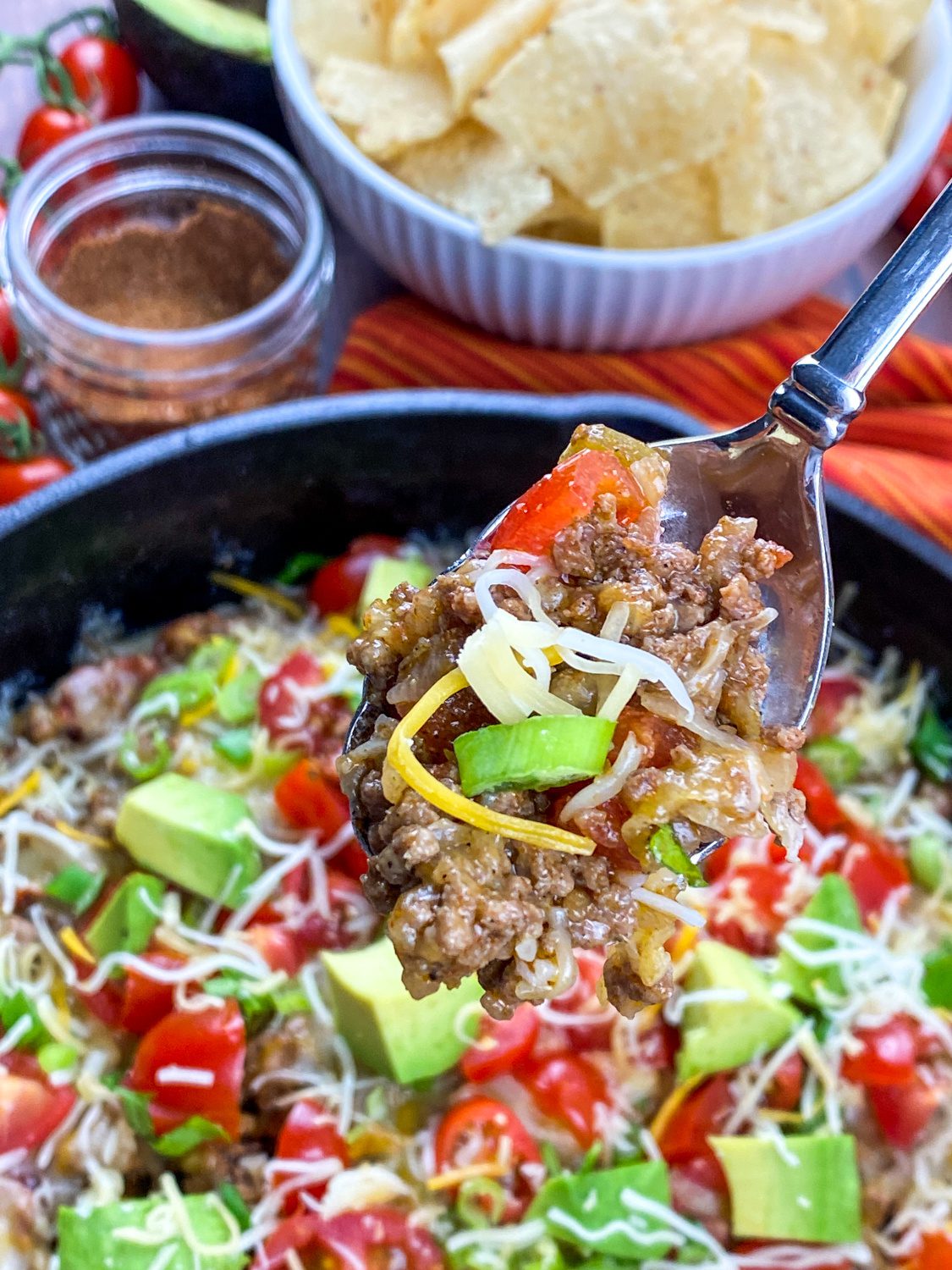 Cheesy beef taco skillet in a cast iron pan with fresh toppings and tortilla chips on the side.