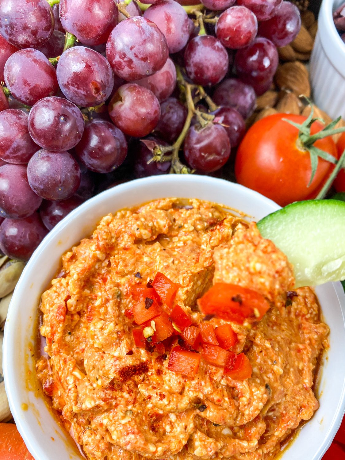 Bowl of spicy feta dip with roasted red peppers and red pepper flakes with a cucumber being dipped