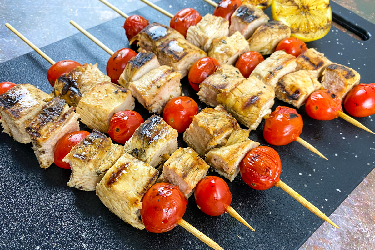 Grilled Greek chicken skewers with tomatoes and lemon on a slate platter