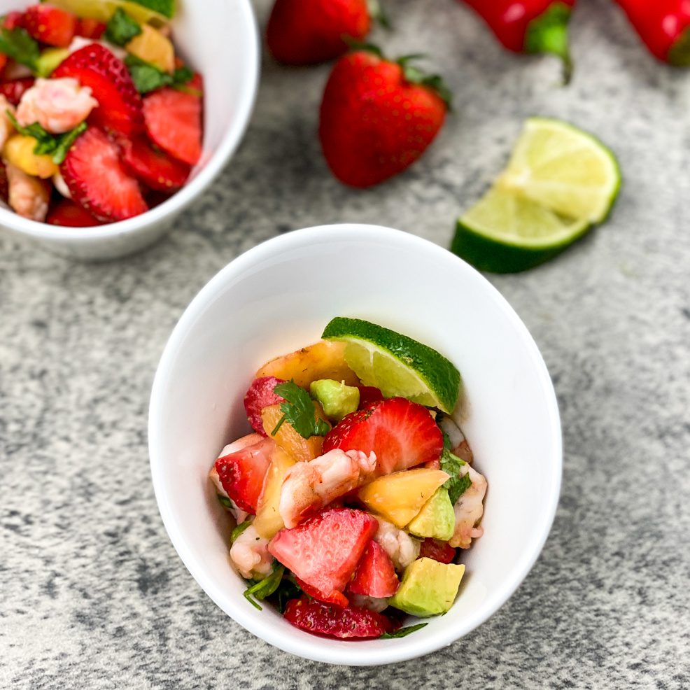 Bowl of colorful strawberry shrimp ceviche with lime wedges