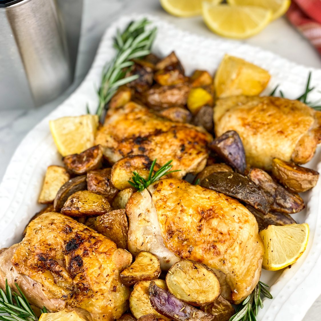 Crispy lemon rosemary chicken thighs with grilled lemon wedges on a serving platter