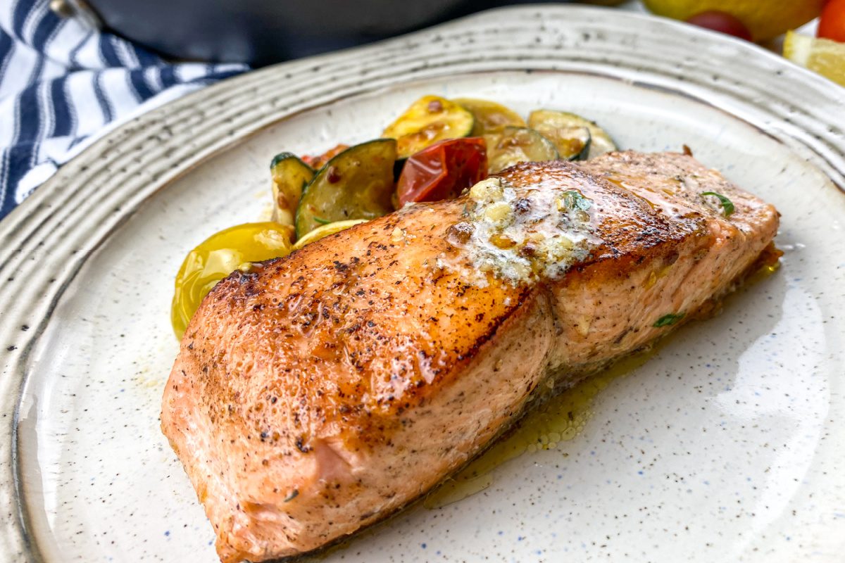 Crispy skin salmon fillets topped with herb butter and sautéed vegetables
