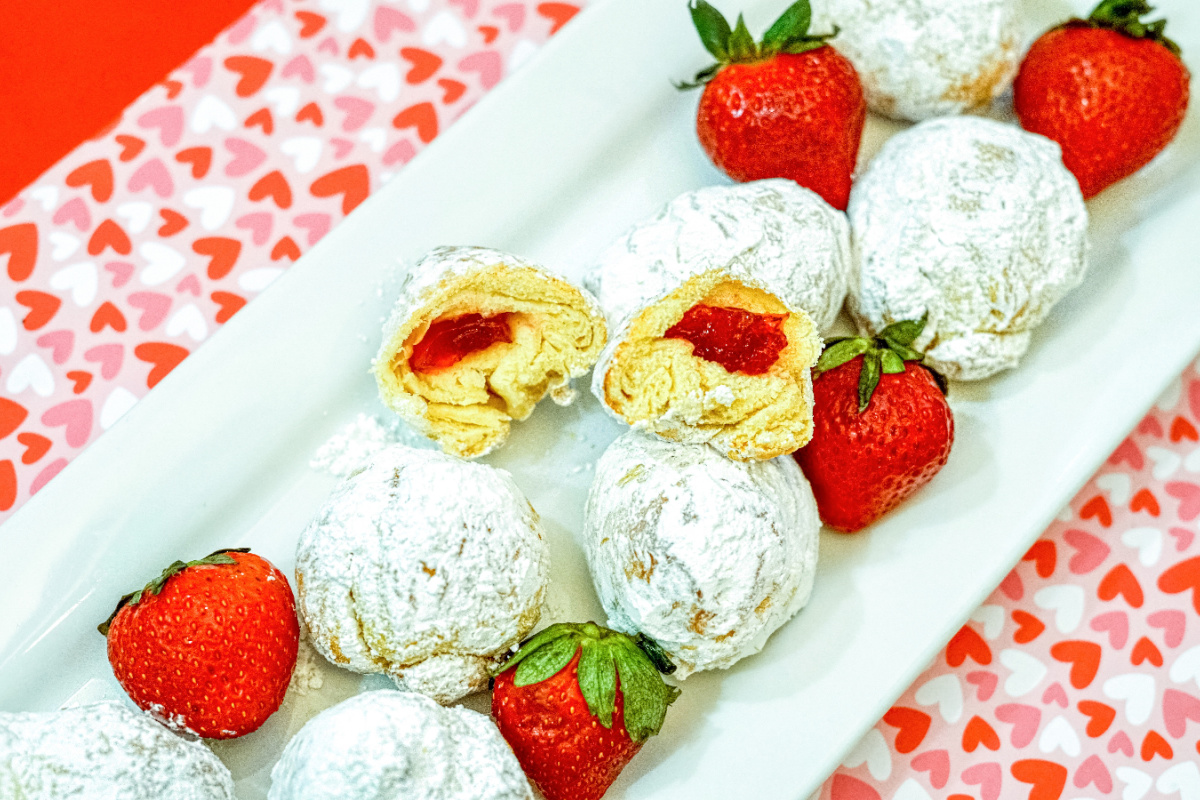Golden air fryer strawberry donut holes dusted with powdered sugar on white platter with fresh strawberries